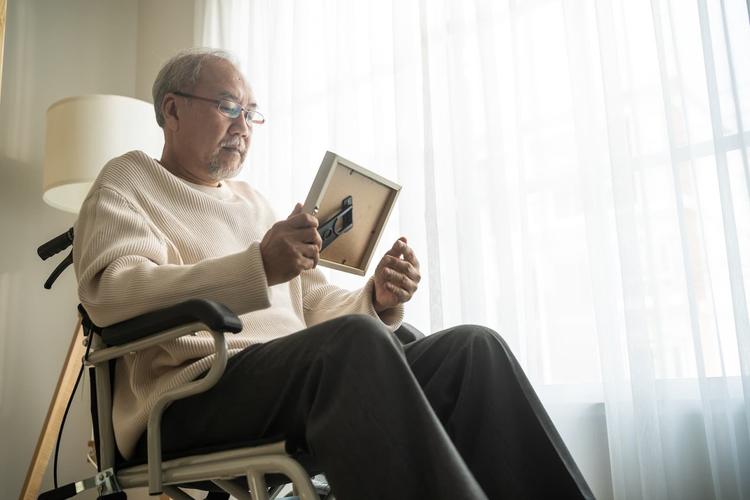 A man sits in a wheelchair in a memory care facility looking at a photograph