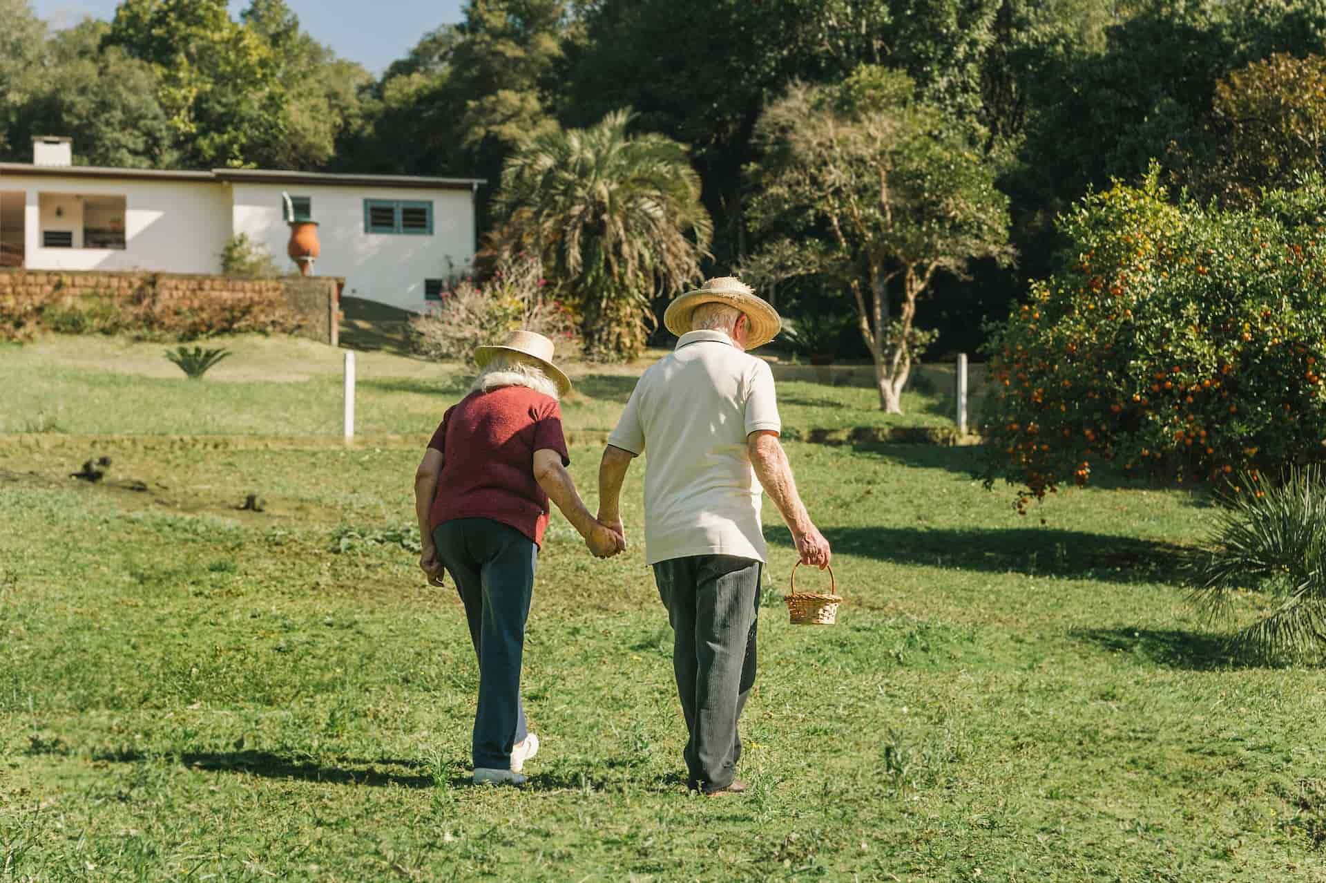 An elderly couple walk hand in hand across grass while in assisted living in Modesto