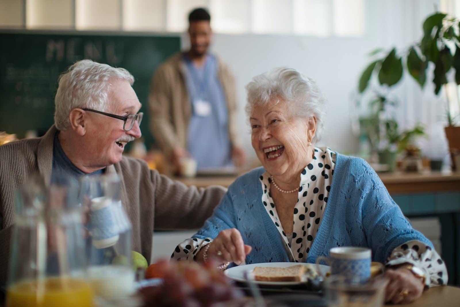Two elderly people laugh together in a senior living care home
