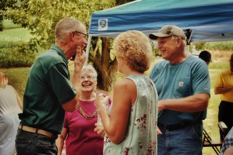 A group of senior citizens laugh and chat together outside by a tent